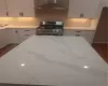 Kitchen with funnel exhaust hood, white cabinetry, dark wood-type flooring, and range