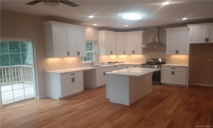 Kitchen with gas range, white cabinets, ceiling fan, and wall chimney exhaust hood