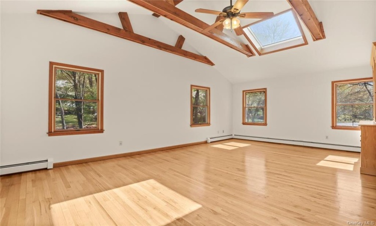 Family room with a vaulted ceiling with custom beams, ceiling fan and skylights.