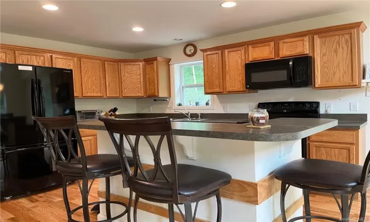 Kitchen with sink, black appliances, light hardwood / wood-style flooring, and a breakfast bar