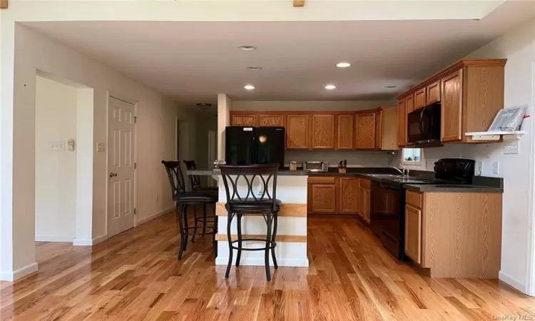 Kitchen with black appliances, sink, light hardwood / wood-style floors, and a kitchen bar