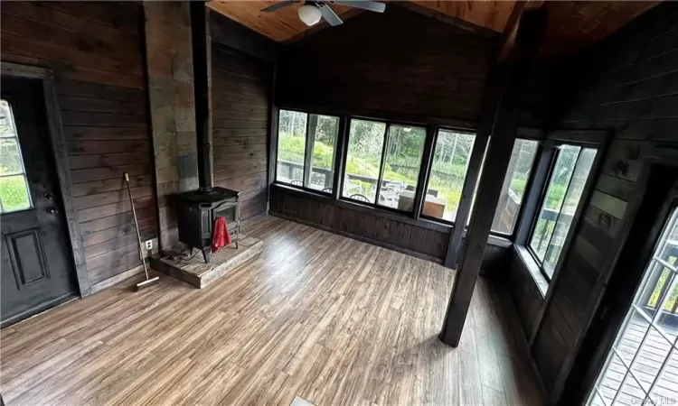 Living room featuring hardwood / wood-style flooring, ceiling fan, a wood stove, wooden ceiling, and wooden walls