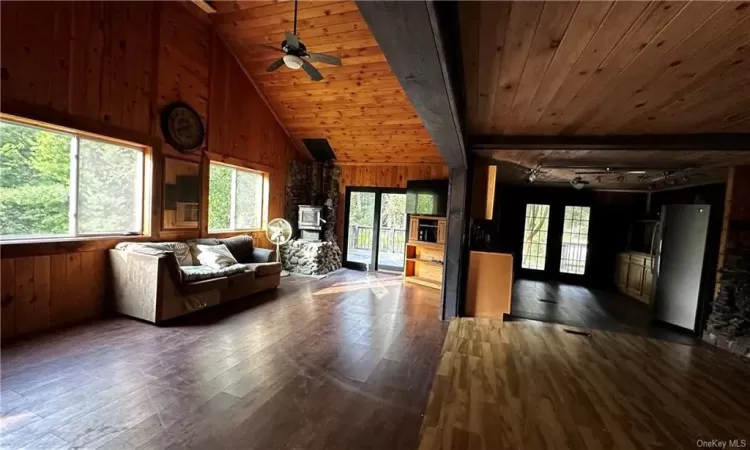 Unfurnished living room with wooden ceiling, ceiling fan, wooden walls, and dark wood-type flooring