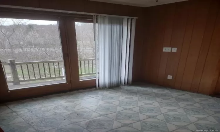 Unfurnished room featuring wooden walls, a healthy amount of sunlight, and light tile floors