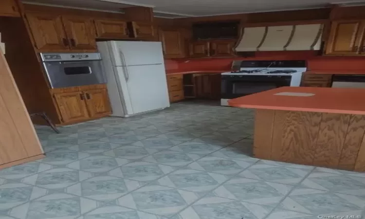 Kitchen with wall chimney exhaust hood, white appliances, and light tile floors