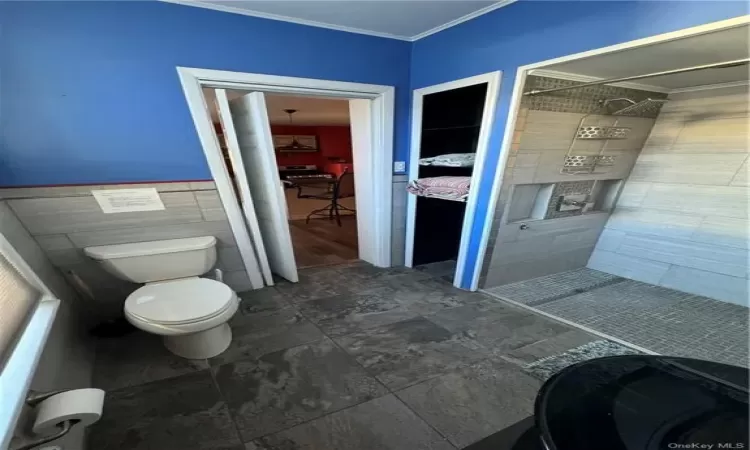 Bathroom with ornamental molding, toilet, tile patterned floors, and tile walls