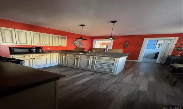 Kitchen featuring range, dark wood-type flooring, cream cabinets, pendant lighting, and sink