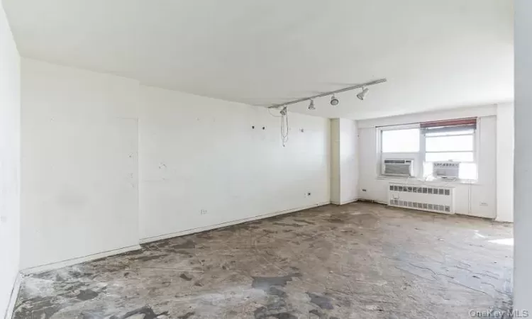 Spare room featuring cooling unit, rail lighting, radiator, and concrete flooring