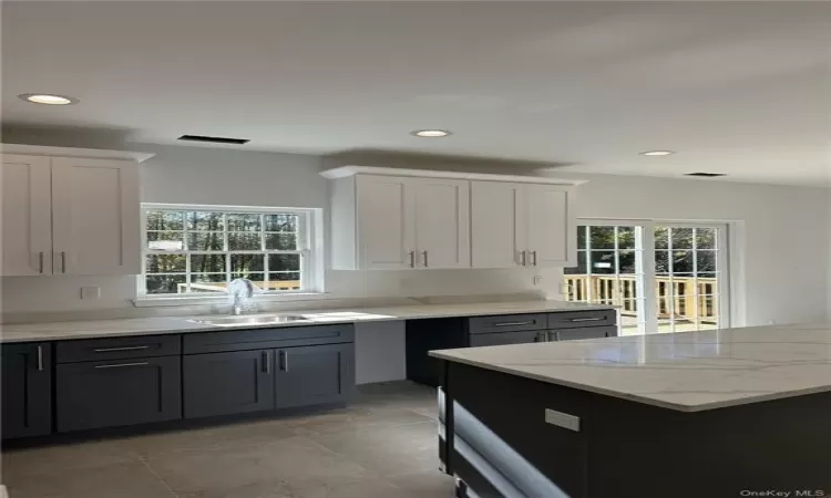 Kitchen with white cabinets, light stone countertops, sink, and light tile patterned floors