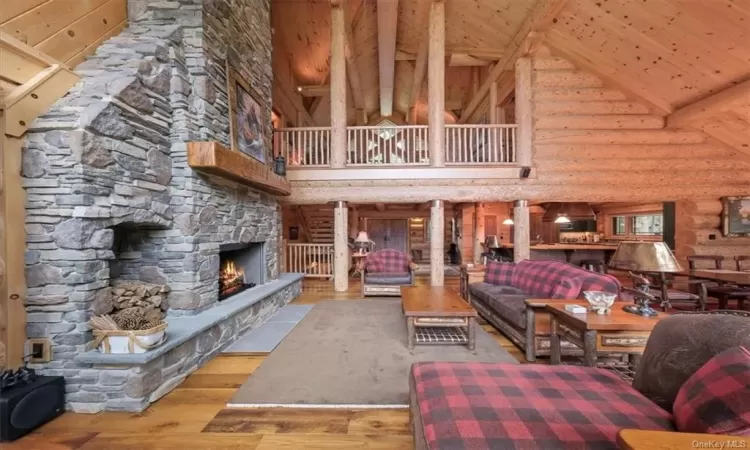 Living room featuring log walls, beamed ceiling, hardwood / wood-style floors, a stone fireplace, and high vaulted ceiling