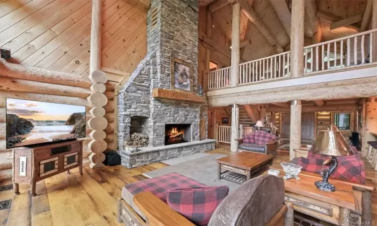 Living room with wood-type flooring, rustic walls, wooden walls, a stone fireplace, and a towering ceiling