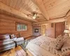 Bedroom with log walls, beamed ceiling, hardwood / wood-style floors, wooden ceiling, and a stone fireplace