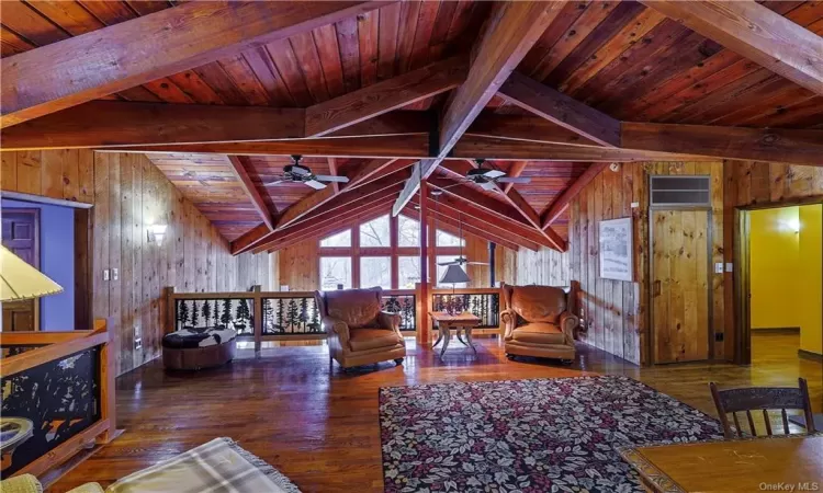 Living room featuring wooden walls, ceiling fan, lofted ceiling with beams, and wood ceiling