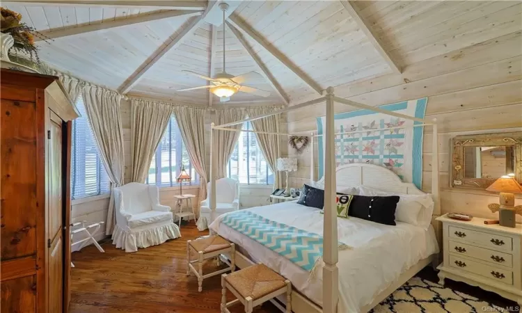 Bedroom with lofted ceiling with beams, hardwood / wood-style flooring, wood walls, wood ceiling, and ceiling fan