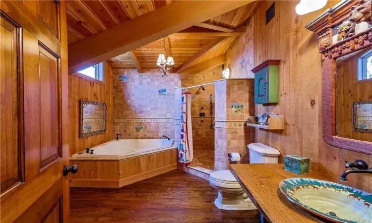 Bathroom with lofted ceiling with beams, wood walls, and hardwood / wood-style flooring