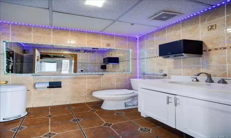 Bathroom with tile floors, a drop ceiling, toilet, and tile walls