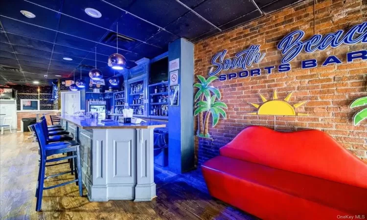 Bar with dark hardwood / wood-style floors and brick wall