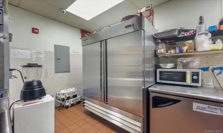 Kitchen with tile walls, a drop ceiling, stainless steel counters, tile flooring, and appliances with stainless steel finishes