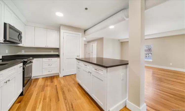 Kitchen with stainless steel appliances, white cabinets, and light wood-type flooring