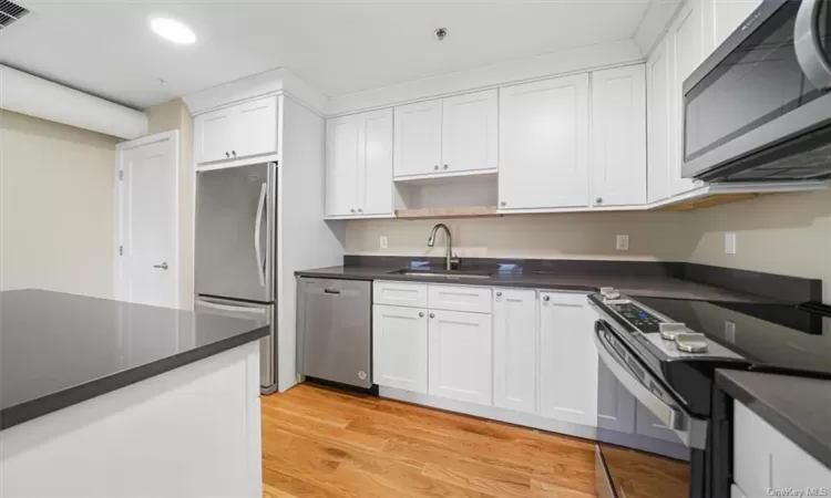 Kitchen with appliances with stainless steel finishes, white cabinetry, sink, and light wood-type flooring