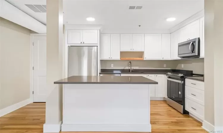 Kitchen with stainless steel appliances, light hardwood / wood-style flooring, white cabinets, and sink