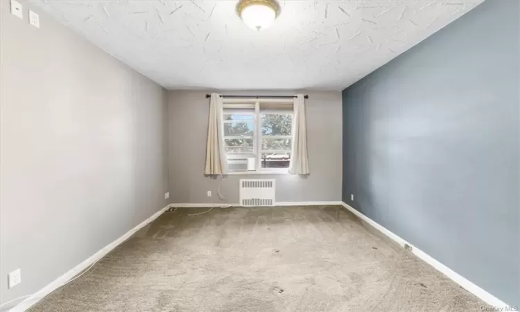 Carpeted spare room with a textured ceiling and radiator heating unit