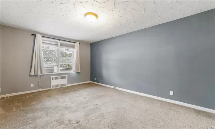 Unfurnished room with a textured ceiling, carpet flooring, and radiator heating unit