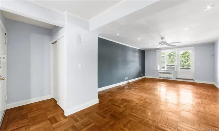 Empty room with crown molding, ceiling fan, radiator heating unit, and parquet flooring