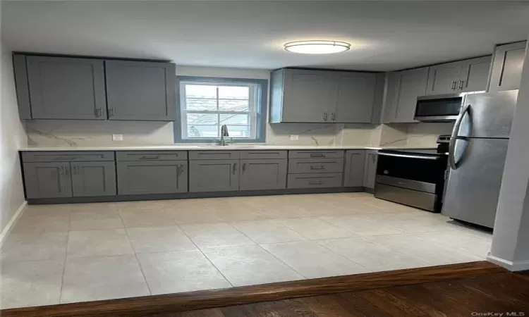 Kitchen with light tile flooring, gray cabinetry, tasteful backsplash, appliances with stainless steel finishes, and sink