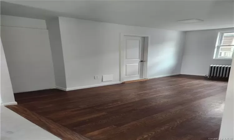 Unfurnished room featuring dark hardwood / wood-style floors and radiator