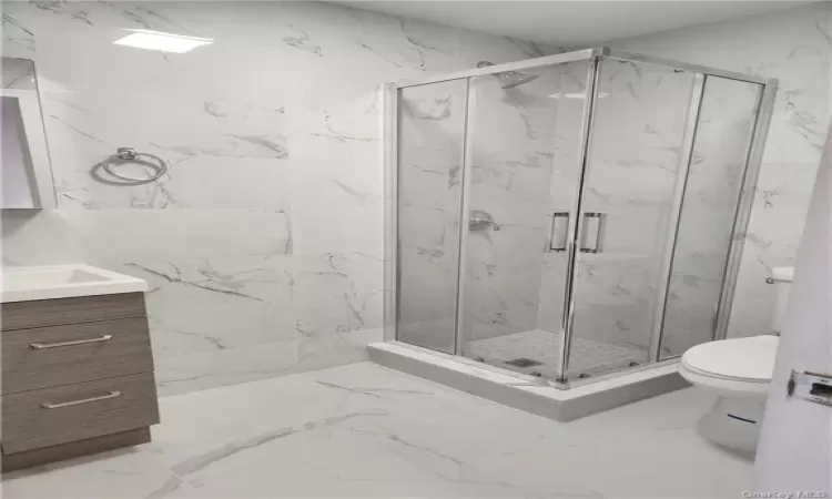 Bathroom featuring a shower with door, toilet, tile floors, and large vanity