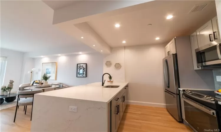 Kitchen with light hardwood / wood-style flooring, kitchen peninsula, light stone countertops, appliances with stainless steel finishes, and sink