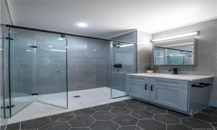 Bathroom with tile walls, tile floors, an enclosed shower, and vanity with extensive cabinet space