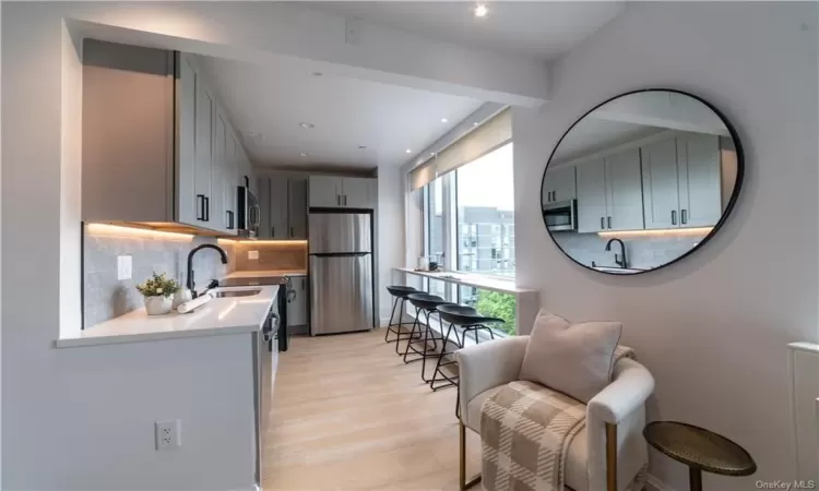 Kitchen featuring light hardwood / wood-style floors, gray cabinetry, tasteful backsplash, appliances with stainless steel finishes, and sink