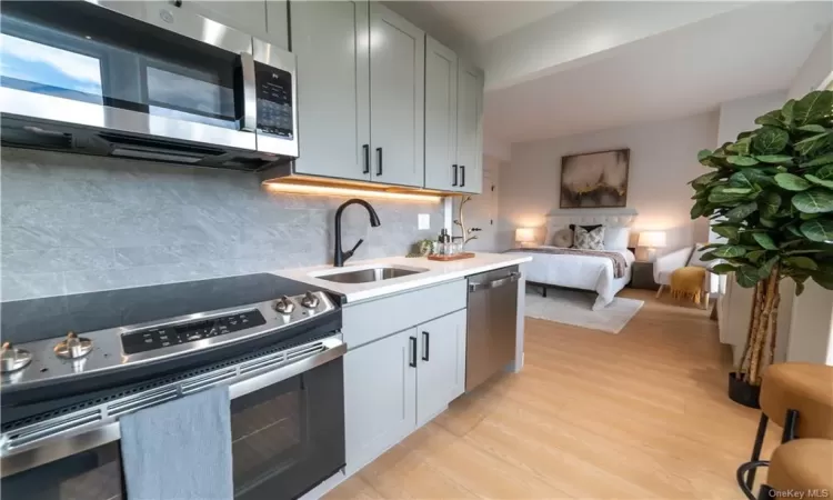 Kitchen with backsplash, appliances with stainless steel finishes, sink, and light wood-type flooring