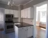 Kitchen with stainless steel appliances, a notable chandelier, backsplash, light tile floors, and radiator