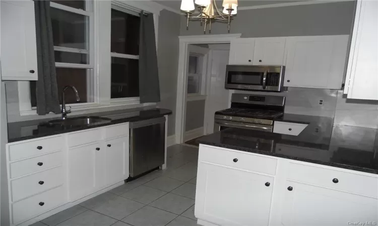 Kitchen with appliances with stainless steel finishes, a chandelier, sink, white cabinetry, and ornamental molding