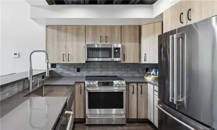 Kitchen with appliances with stainless steel finishes, sink, tasteful backsplash, and dark wood-type flooring