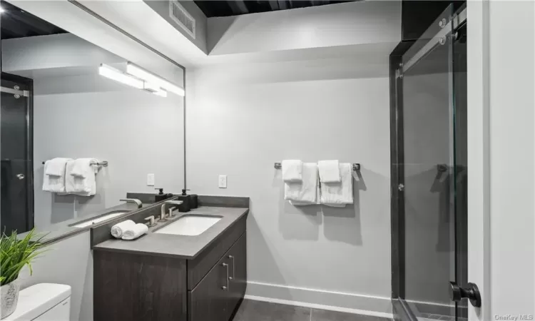 Bathroom with tile flooring, vanity with extensive cabinet space, a shower with shower door, and toilet