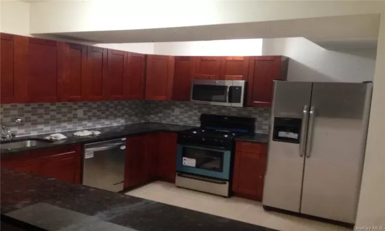 Kitchen featuring dark stone counters, light tile flooring, tasteful backsplash, appliances with stainless steel finishes, and sink