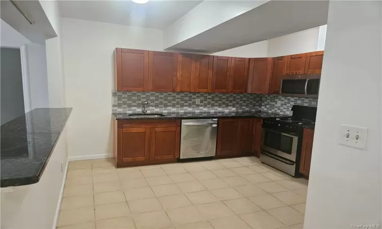 Kitchen featuring stainless steel appliances, sink, backsplash, light tile patterned floors, and dark stone countertops