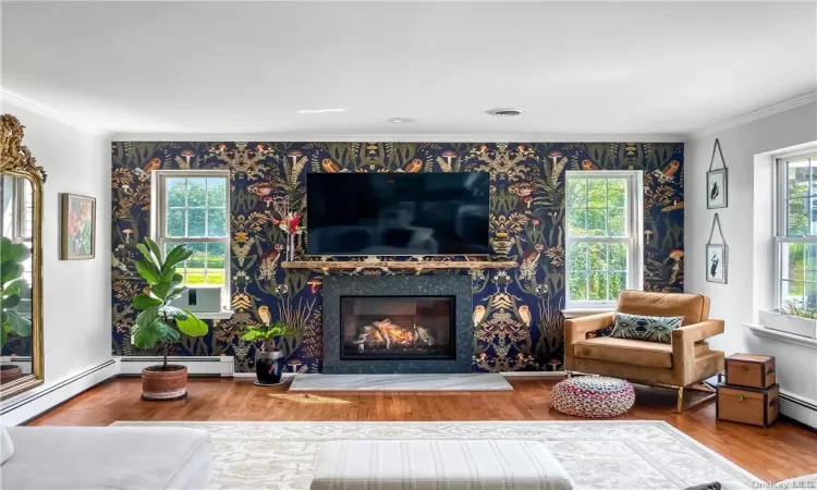 Living room with crown molding, a fireplace, baseboard heating, and wood-type flooring