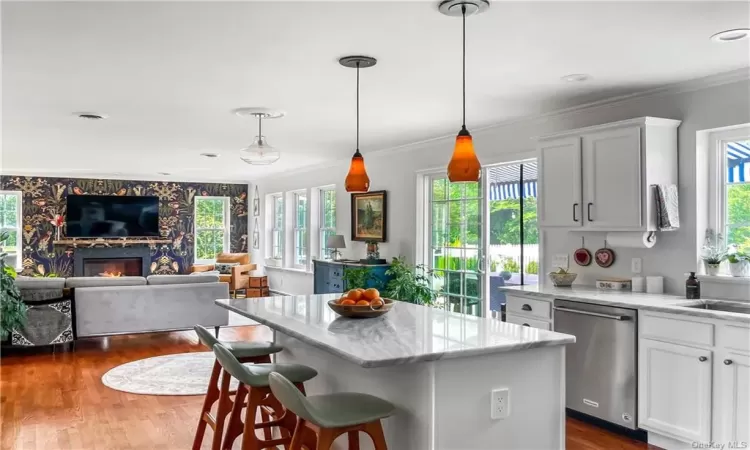 Kitchen with white cabinetry, a fireplace, hardwood / wood-style flooring, pendant lighting, and dishwasher