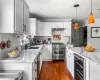 Kitchen featuring dark wood-type flooring, appliances with stainless steel finishes, light stone counters, wine cooler, and pendant lighting