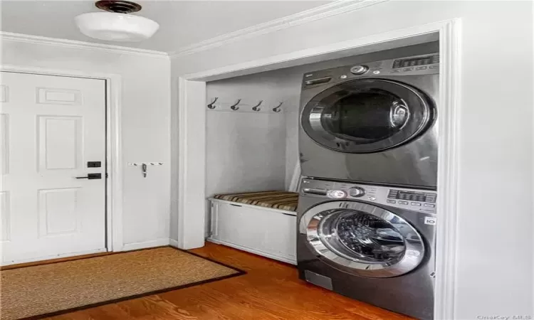 Washroom with hardwood / wood-style floors, stacked washer and dryer, and crown molding