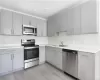 Kitchen with stainless steel appliances, sink, light wood-type flooring, and gray cabinets