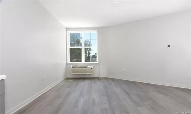 Unfurnished room featuring wood-type flooring and a wall mounted air conditioner