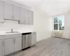 Kitchen featuring light hardwood / wood-style floors, gray cabinets, an AC wall unit, sink, and dishwasher