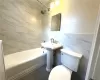 Bathroom with tile floors, tile walls, toilet, and tiled shower / bath combo