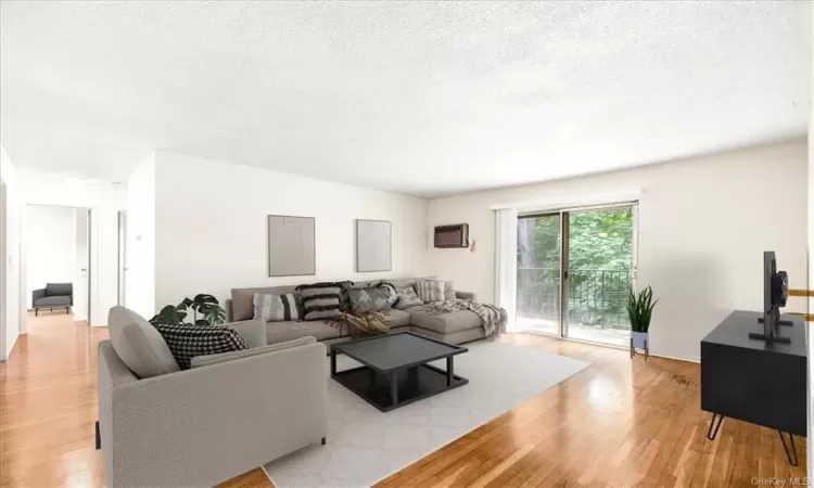 Virtually staged. Living room featuring light hardwood / wood-style flooring, a textured ceiling, and a wall mounted air conditioner.